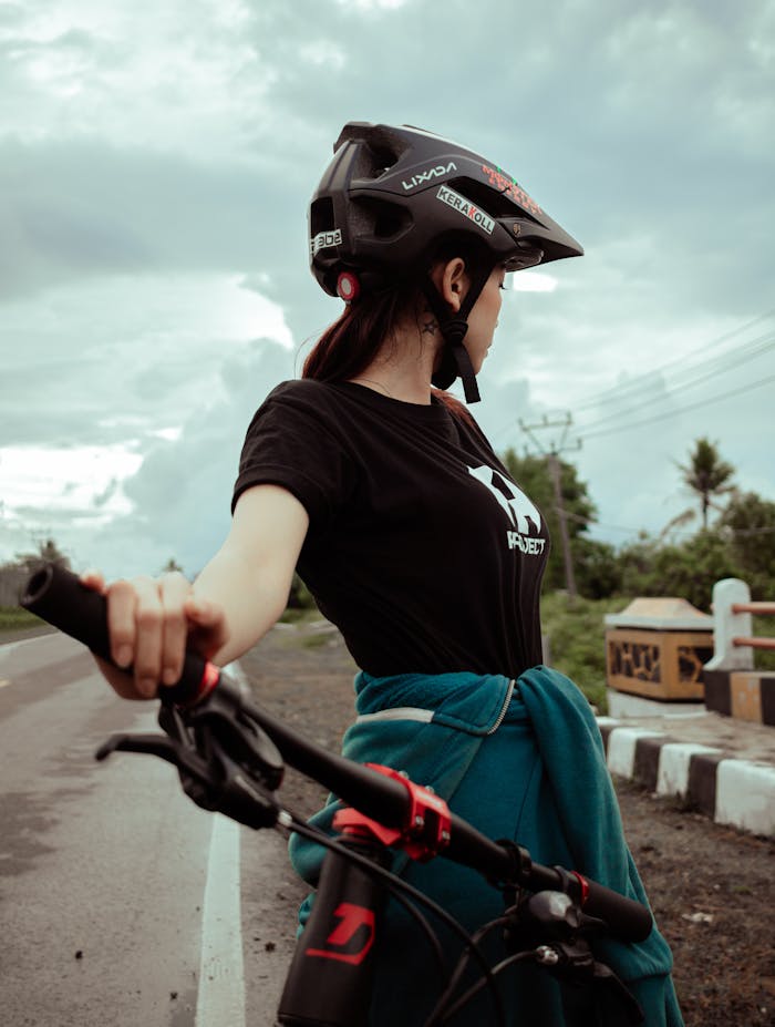 Side view of a woman cyclist on an open road, wearing a helmet and ready to ride, promoting safety.